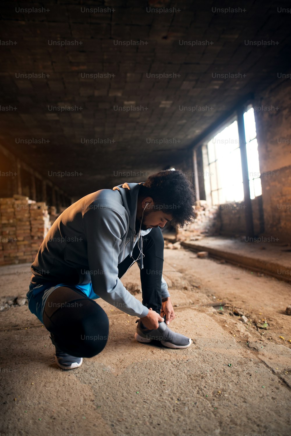 Close up view of sporty active afro american runner man crouching and tying velcro sneakers in the abandon sunny place.