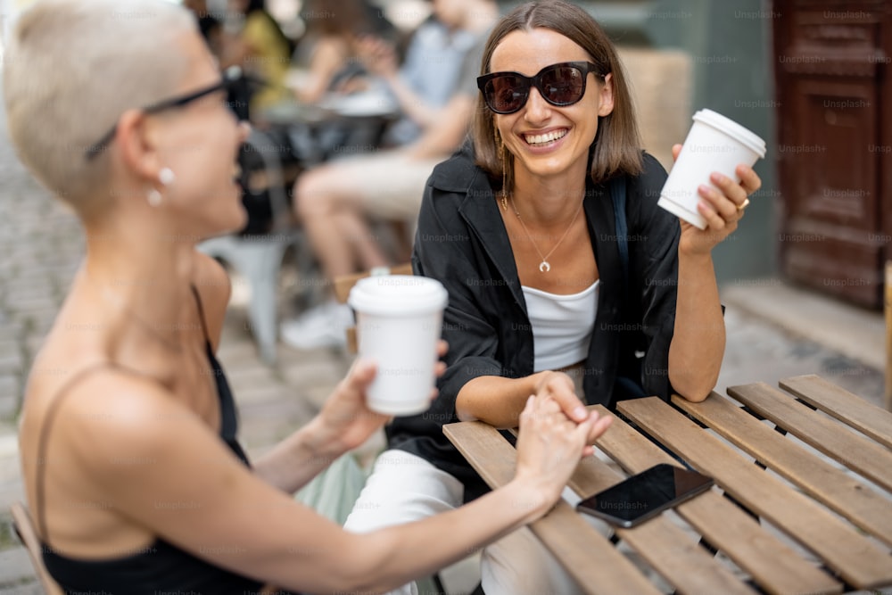 Stylish female couple having fun, drinking coffee at cafe outdoors. Homosexual relation and leisure time in the city