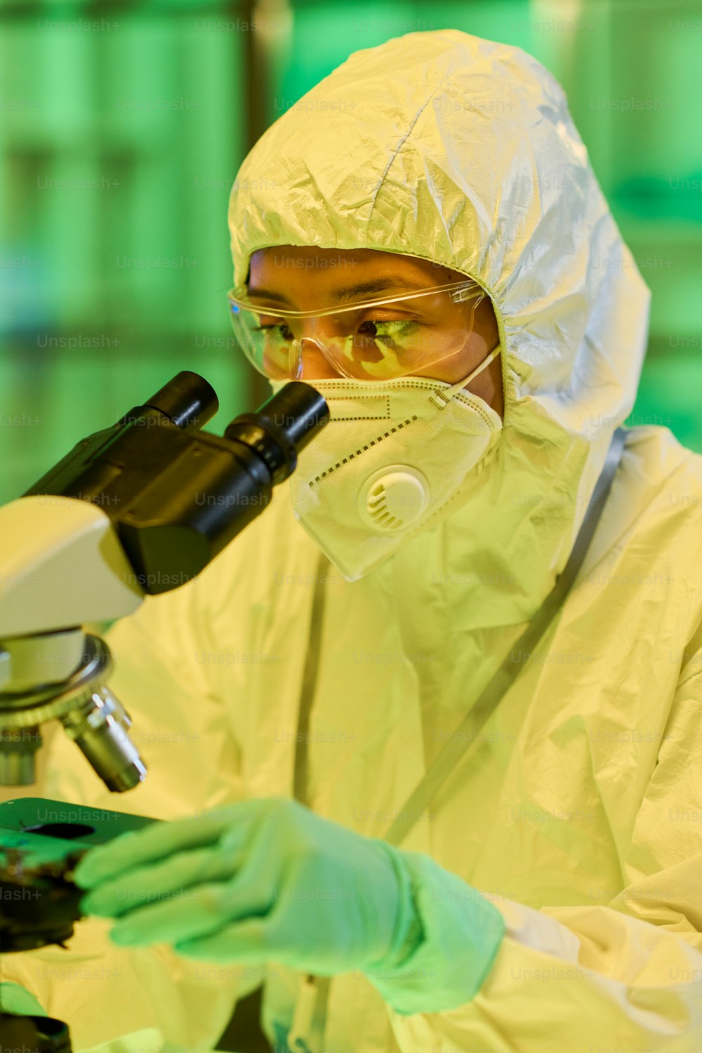 Serious young female biochemist looking in microscope in modern scientific laboratory while studying new strain of coronavirus