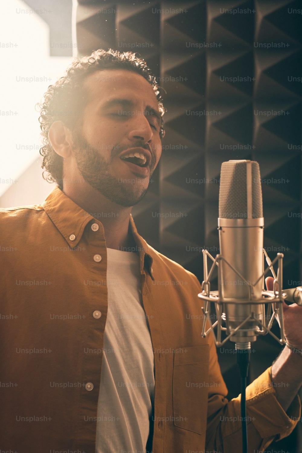 Retrato do homem marroquino na camisa amarela cantando com microfone no estúdio de gravação profissional