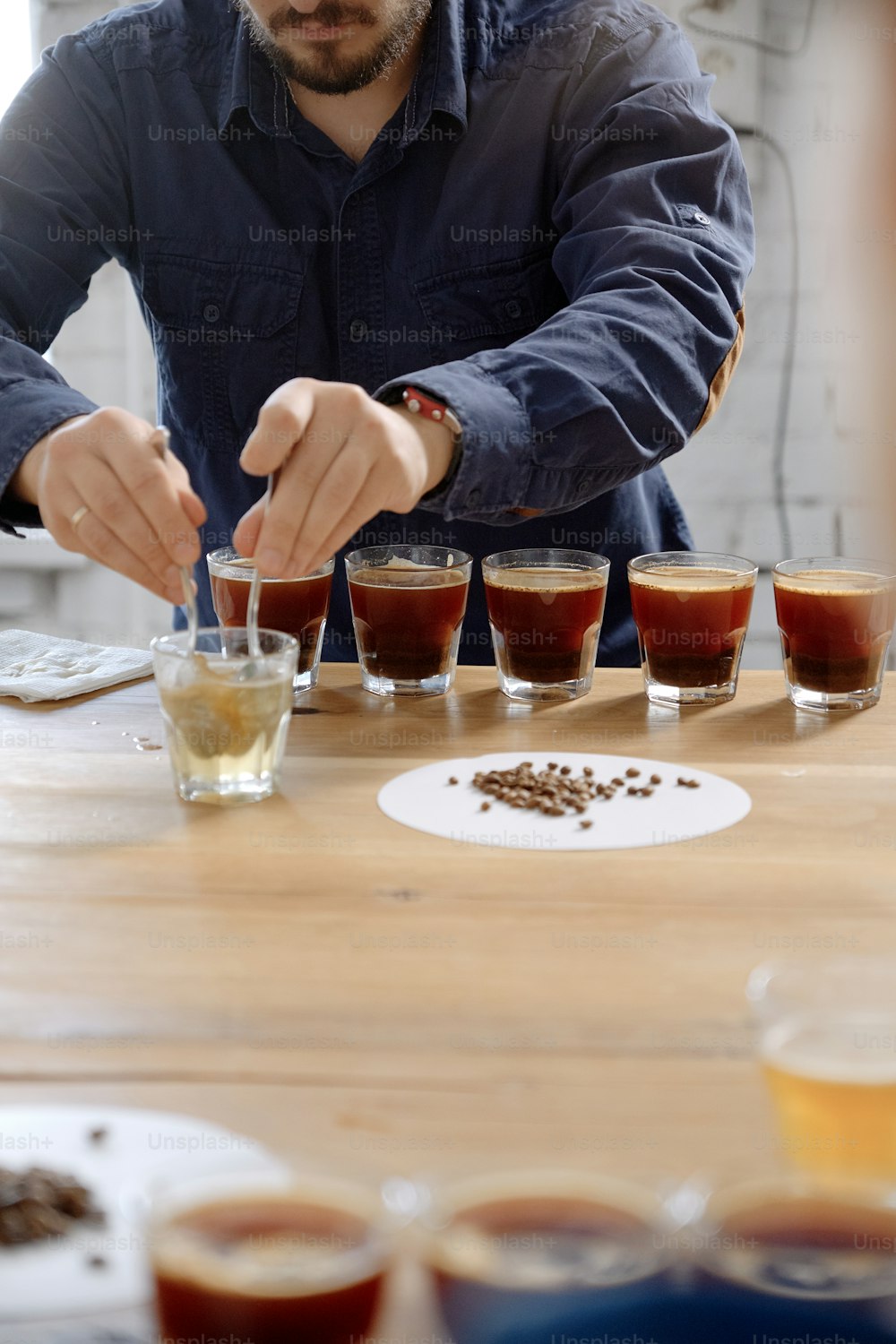 Primer plano de las manos del hombre probando café recién hecho en taza de vidrio, usando cuchara, examinando el sabor y el sabor del café en la prueba de cata de café para barosta
