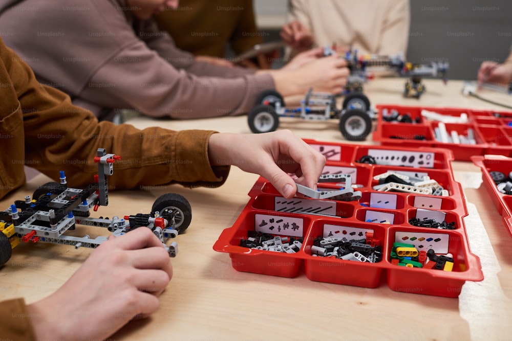 Close-up de crianças sentadas à mesa e construindo carros robóticos do construtor na escola de ciências