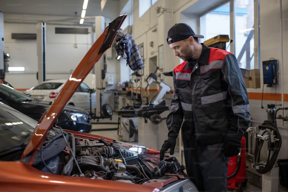 Side view portrait of male mechanic inspecting engine while working in car repair shop, copy space