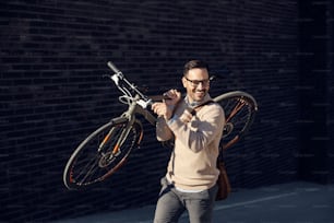 Un hombre a la moda lleva una bicicleta en el hombro en la calle de la ciudad.