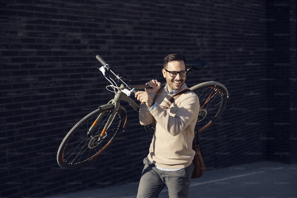 A fashionable man carries bike on the shoulder on the city street.