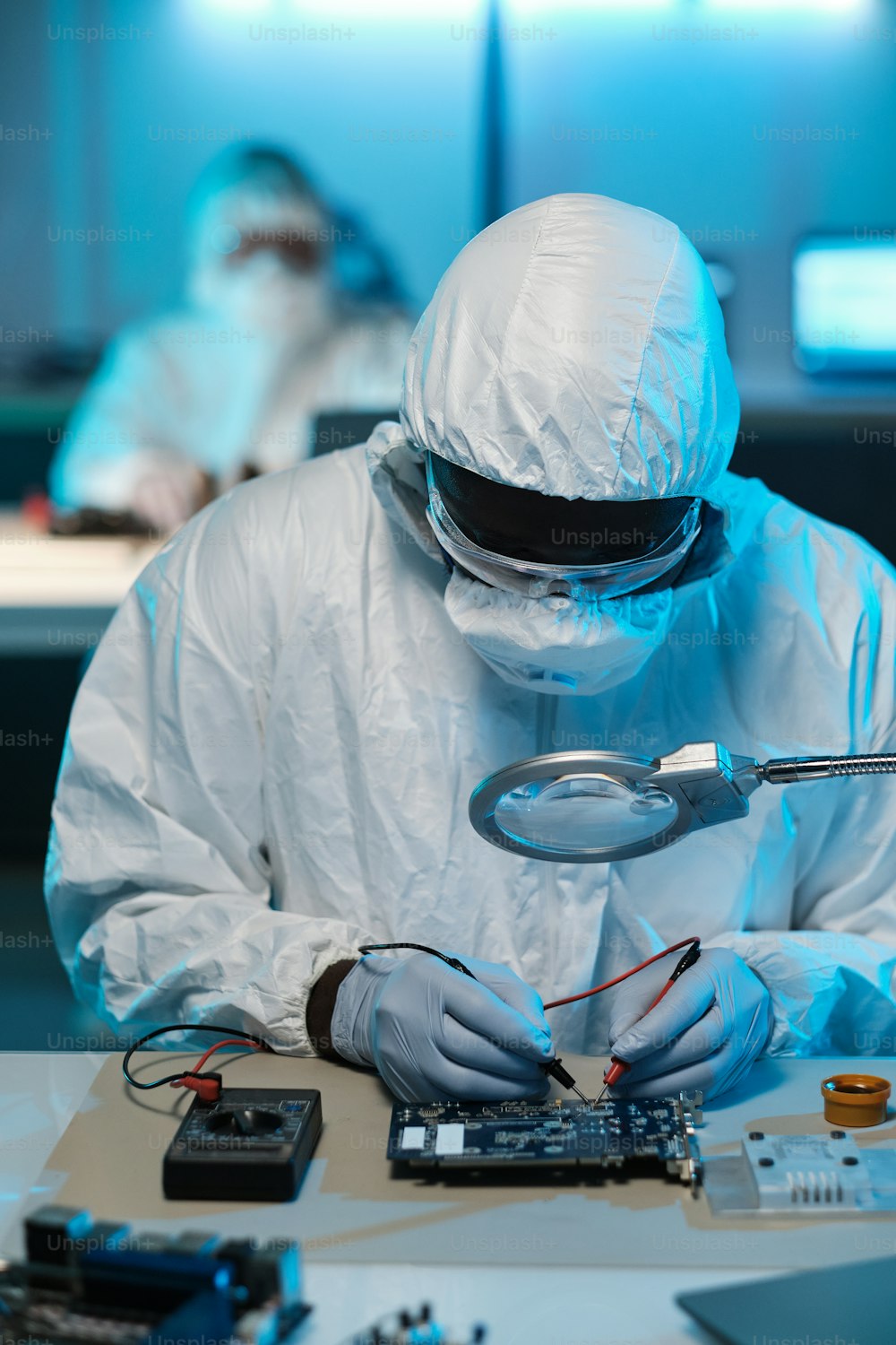 Contemporary repairman in protective workwear soldering circuit board while looking in magnifying glass