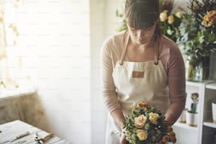 Young woman putting together a bouquet of mixed flowers while working at a table in her flower shop