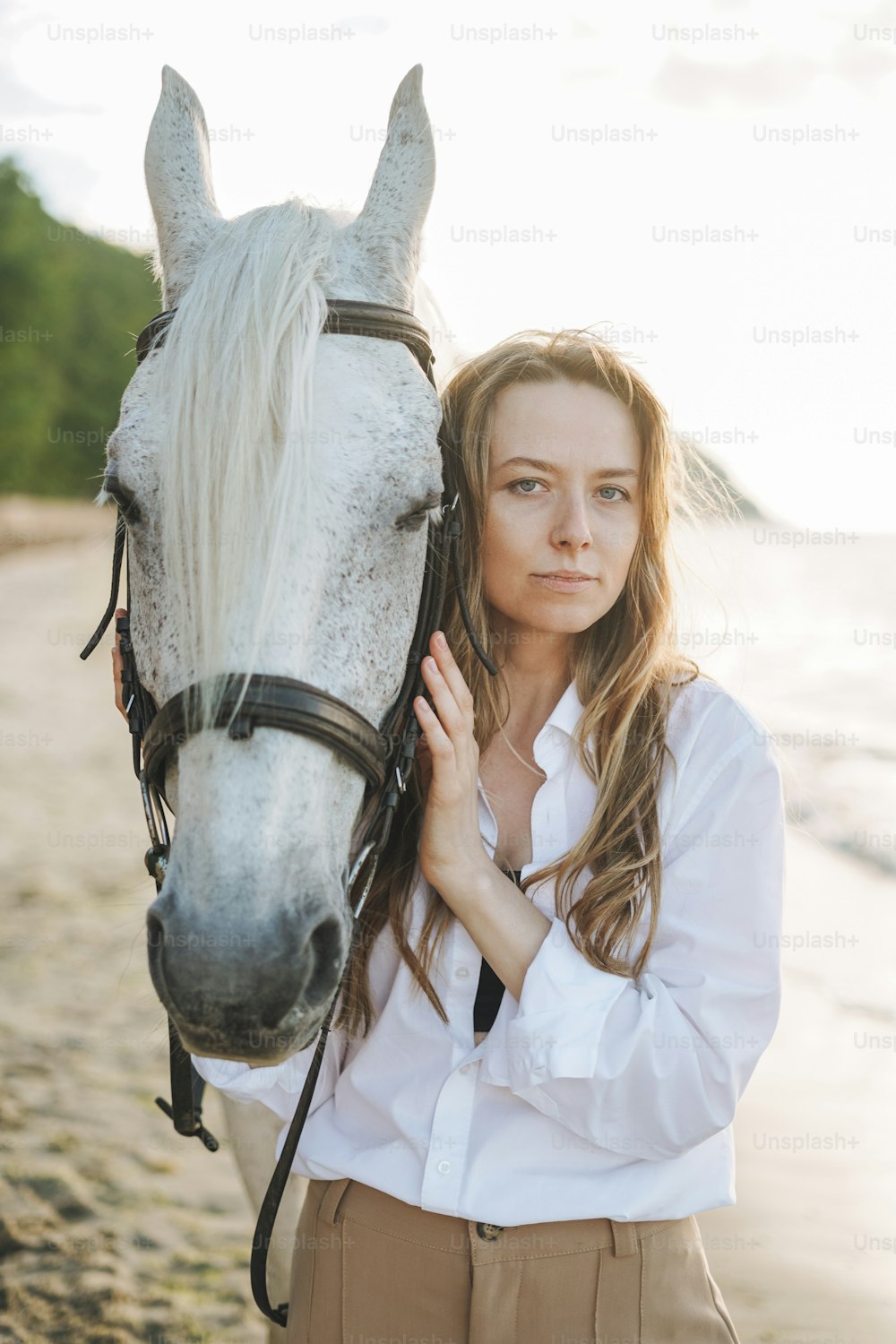 Junge langhaarige Frau im weißen Hemd mit weißem Pferd auf Seelandschaftshintergrund