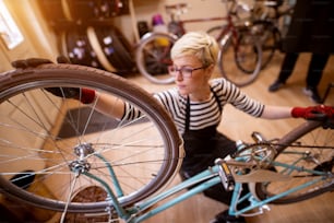 Donna attraente concentrata che controlla l'equilibrio della ruota della bicicletta nel garage soleggiato.