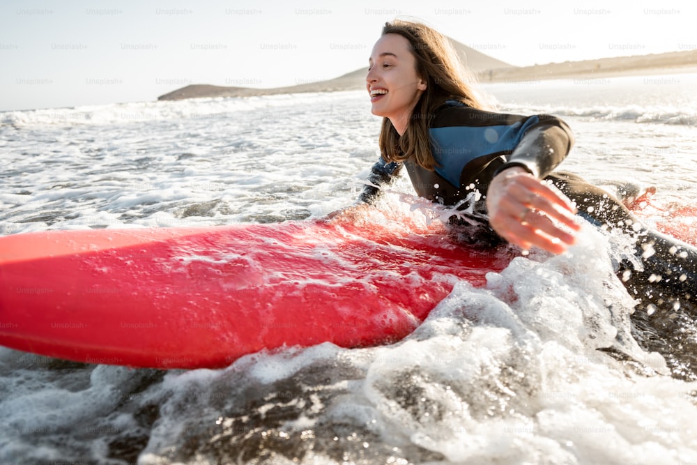 Mujer joven en traje de neopreno que atrapa el flujo de agua en la tabla de surf, surfeando en el océano ondulado durante una puesta de sol. Concepto de deportes acuáticos y estilo de vida activo