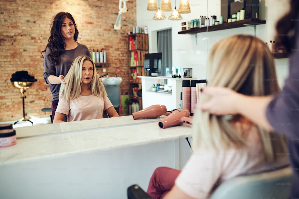 Young blonde woman sitting in a chair talking with her hairstylist while having her hair done during a salon appointment