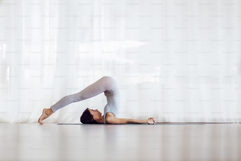 Vista lateral de la chica yogui delgada en forma en la postura de yoga del arado. Interior del estudio de yoga.
