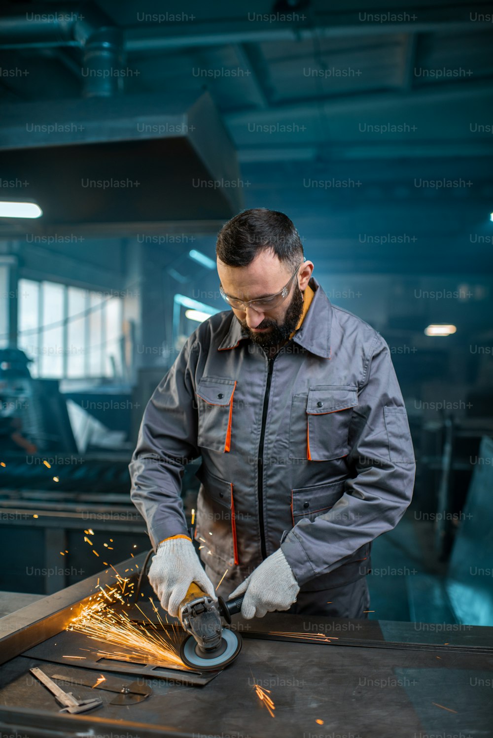 作業着に身を包み、工場で鉄鋼製品を研削する金属加工をしている金属産業の労働者。金属製品の製造におけるハンサムな職人。高品質の写真