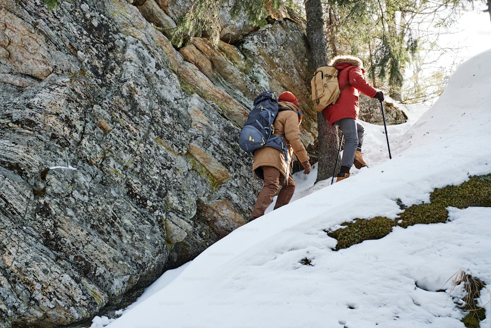 Dois jovens irreconhecíveis usando mochilas caminhando juntos nas montanhas no dia de inverno, tiro de visão de baixo ângulo