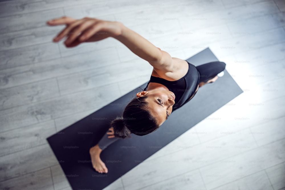 Vista dall'alto della bella bruna in forma in piedi sul tappetino nello studio di yoga in posizione yoga Exalted Crescent Lunge.
