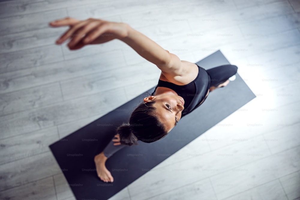 Top view of fit beautiful brunette standing on the mat in yoga studio in Exalted Crescent Lunge yoga pose.