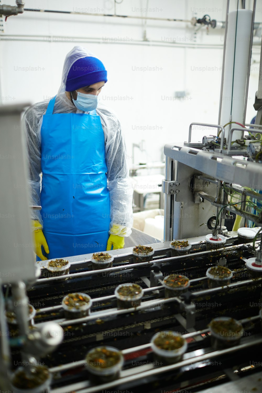 Young controller in uniform looking at seaweed salad in plastic containers on producing line