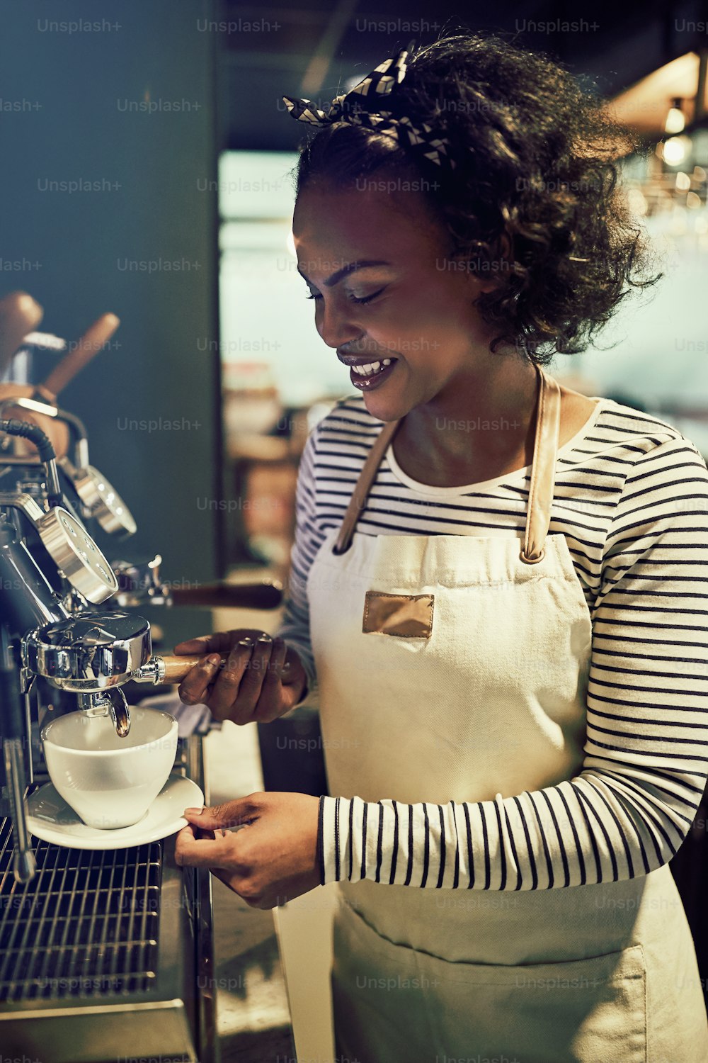 Smiling young African barista pouring a cup of fresh coffee while standing at a coffee maker in a trendy cafe