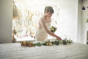 Young female florist arranging a bouquet of mixed flowers while standing at a table in her flower workshop