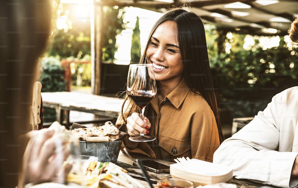 Happy asian woman drinking red wine sitting at restaurant dining table - Group of friends having bbq dinner party outside - Food and beverage lifestyle concept