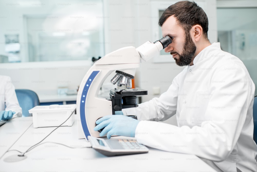 Man in medical uniform working with microscope making analysis at the laboratory office