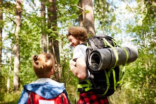 Father and son scouts with backpacks walking in the forest to their camp on sunny day