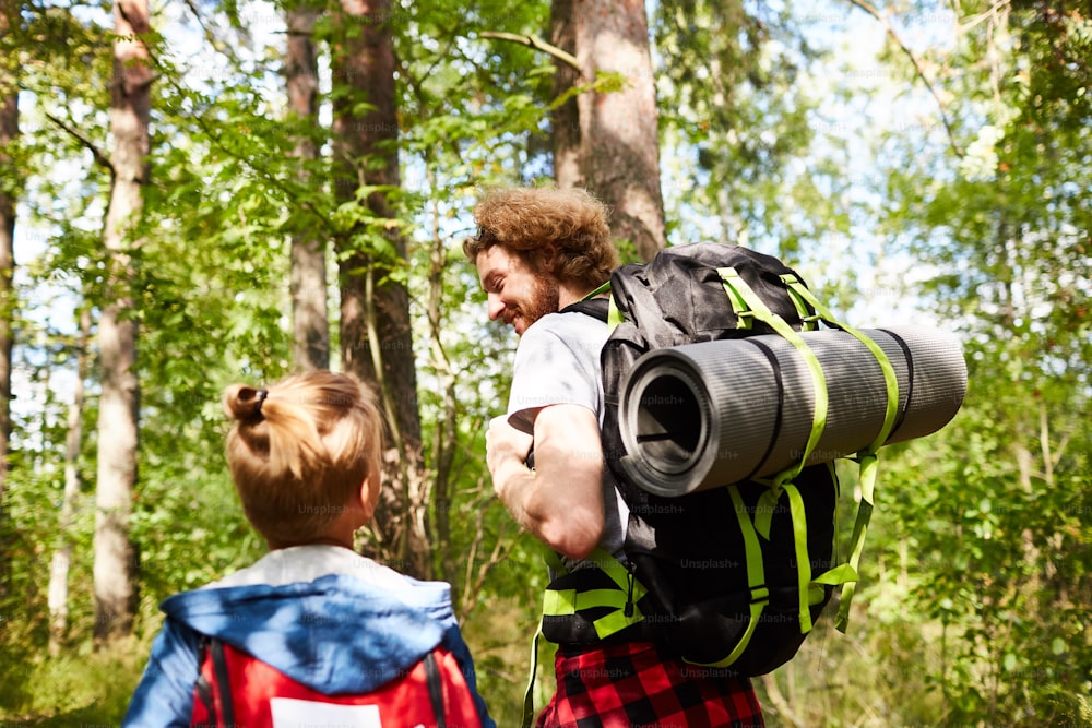Father and son scouts with backpacks walking in the forest to their camp on sunny day