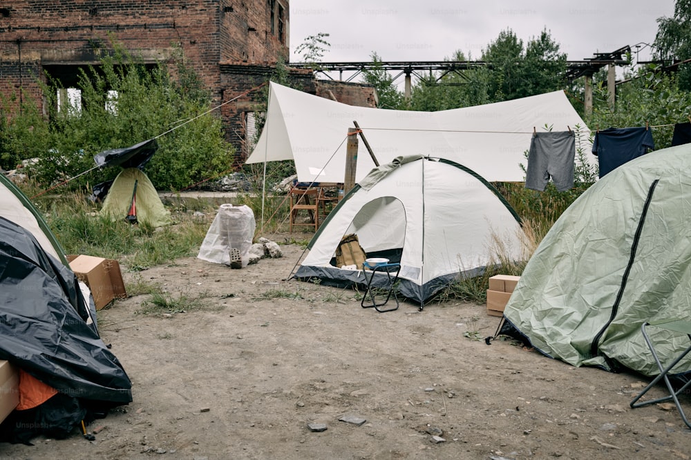 Refugee camp with tents, clothes hanging on rope and folding chairs against abandoned building