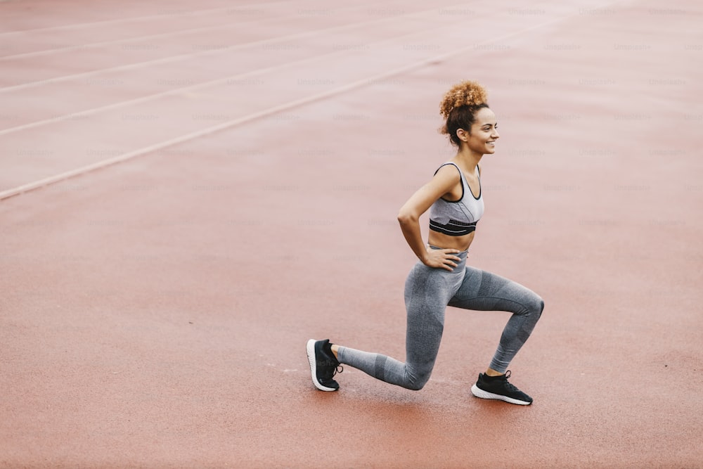 A fit sportswoman with healthy habits is doing lunges in the stadium on wet weather. A sportswoman exercising in the stadium.
