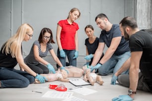 실내에서 훈련하는 동안 인형으로 응급 처치 심장 압박을 하는 방법을 배우는 사람들의 그룹