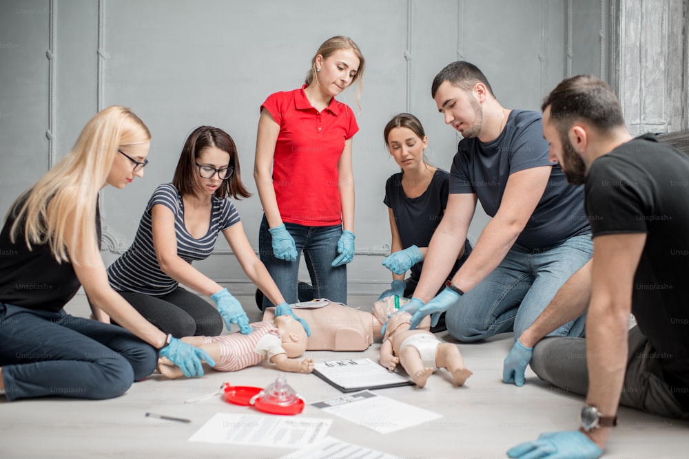 Group of people learning how to make first aid heart compressions with dummies during the training indoors