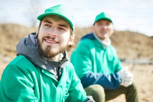 Bearded guy in green uniform and his colleague having rest after work in natural environment