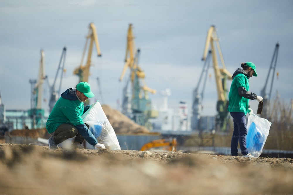 Two young men picking up litter on construction site and putting it into sacks