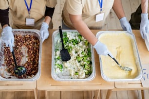 Gloved females standing by table with cooked free food in containers