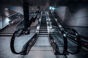 Eine frontale Weitwinkelaufnahme von zwei Rolltreppen in einem Einkaufszentrum oder einem Flughafenterminal oder einem Depot einer Transportstation mit einer Treppe auf der linken Seite; Neonlicht, leuchtende LED-Deckenleuchten