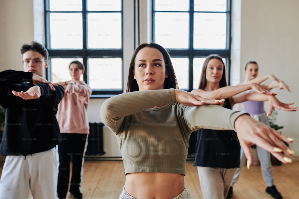 かなりブルネットの10代の女の子と他の十代の若者たちは、パフォーマンスチームのインストラクターやリーダーの後に新しい流行のダンスの動きを繰り返します
