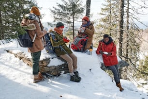 Gruppe stilvoller junger schwarzer und kaukasischer Freunde, die am Wintertag zusammen in den Bergen wandern und Mittagspause machen