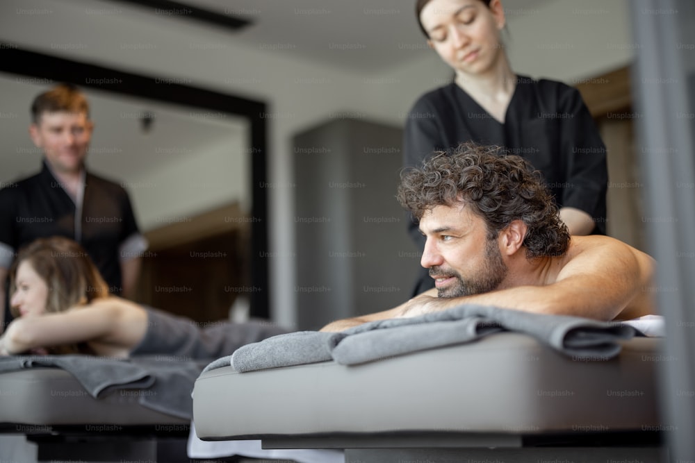 Beau couple allongé dans un salon de spa profitant d’un massage profond du dos et d’une relaxation. Bien-être et loisirs pour les soins de santé ensemble. Concentrez-vous sur l’homme.
