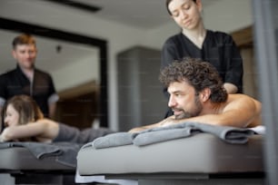 Beautiful couple lying in a spa salon enjoying getting deep back massage and relaxation. Wellness and leisure time for health care together. Focus on the man. Natural light.