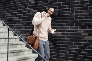 Um homem urbano nas escadas falando ao telefone e tomando café para ir.