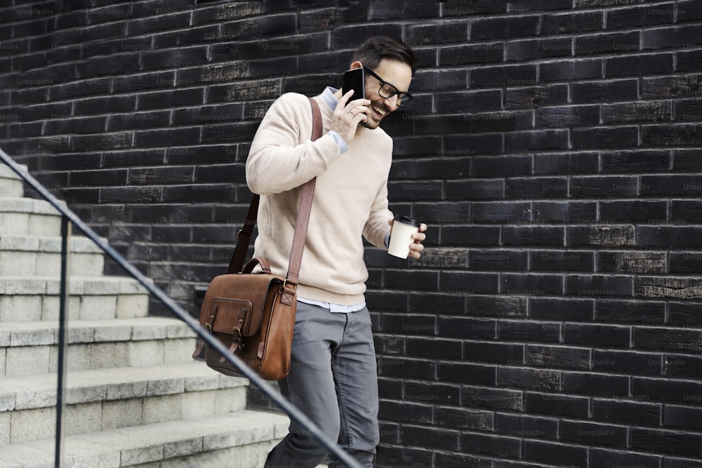 Un hombre urbano en las escaleras hablando por teléfono y tomando café para llevar.