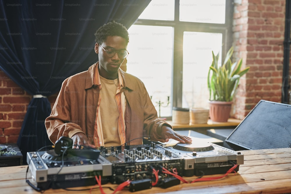 若い深刻な黒人男性は、DJボードを見ながら、調整音楽機器と演奏前にターンテーブルに触れる
