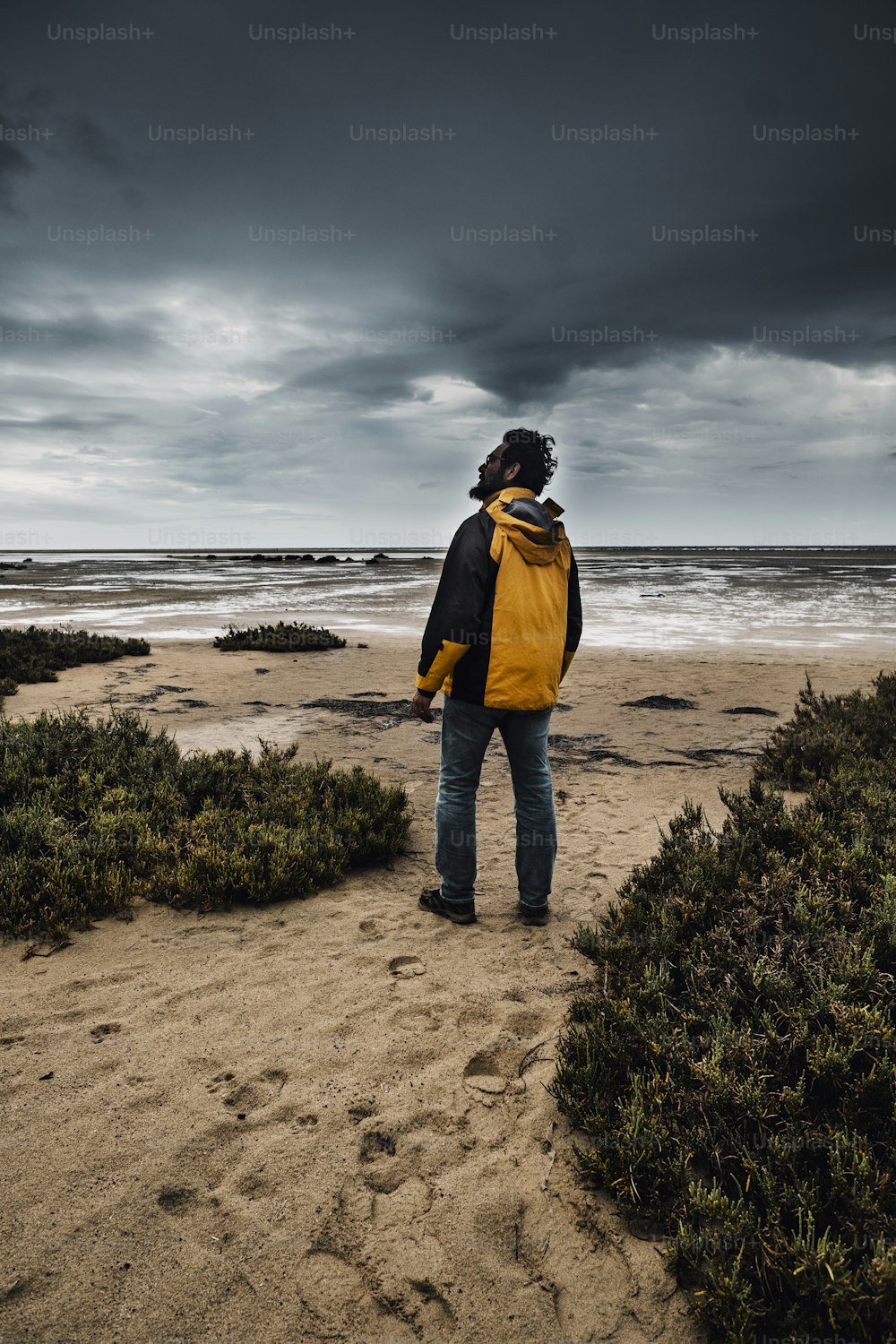 Homem épico em pé contra o mau tempo e nuvens negras ao fundo na praia. Temporada de inverno aventura atividade de lazer conceito de pessoas.