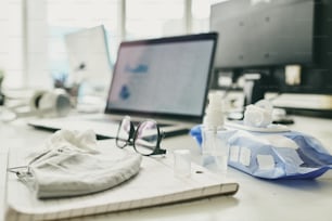 Close-up of wet wipe package, eyeglasses, sanitizer bottle with dispenser and cloth mask on notepad placed on desk