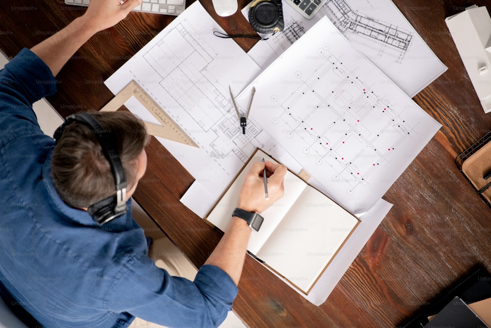 Top view of professional engineer with notebook and pencil sitting by table and going to make working notes or write down new ideas