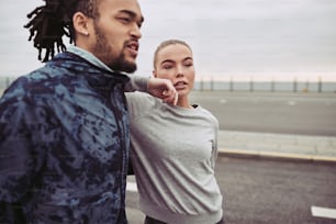 Diverse young couple in sportswear standing together on a road taking a break from a run on an overcast day