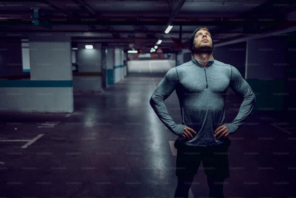 Attractive fit caucasian sportsman in active wear standing in garage with hands on hips and resting.