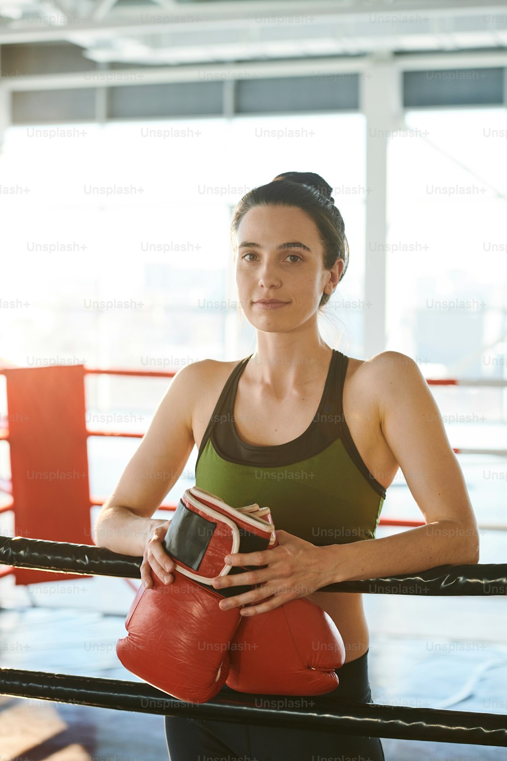 ボクシンググローブを持つかなり若いブルネットの女性は、競争の前にリング上でスポーツトレーニングをする準備ができています