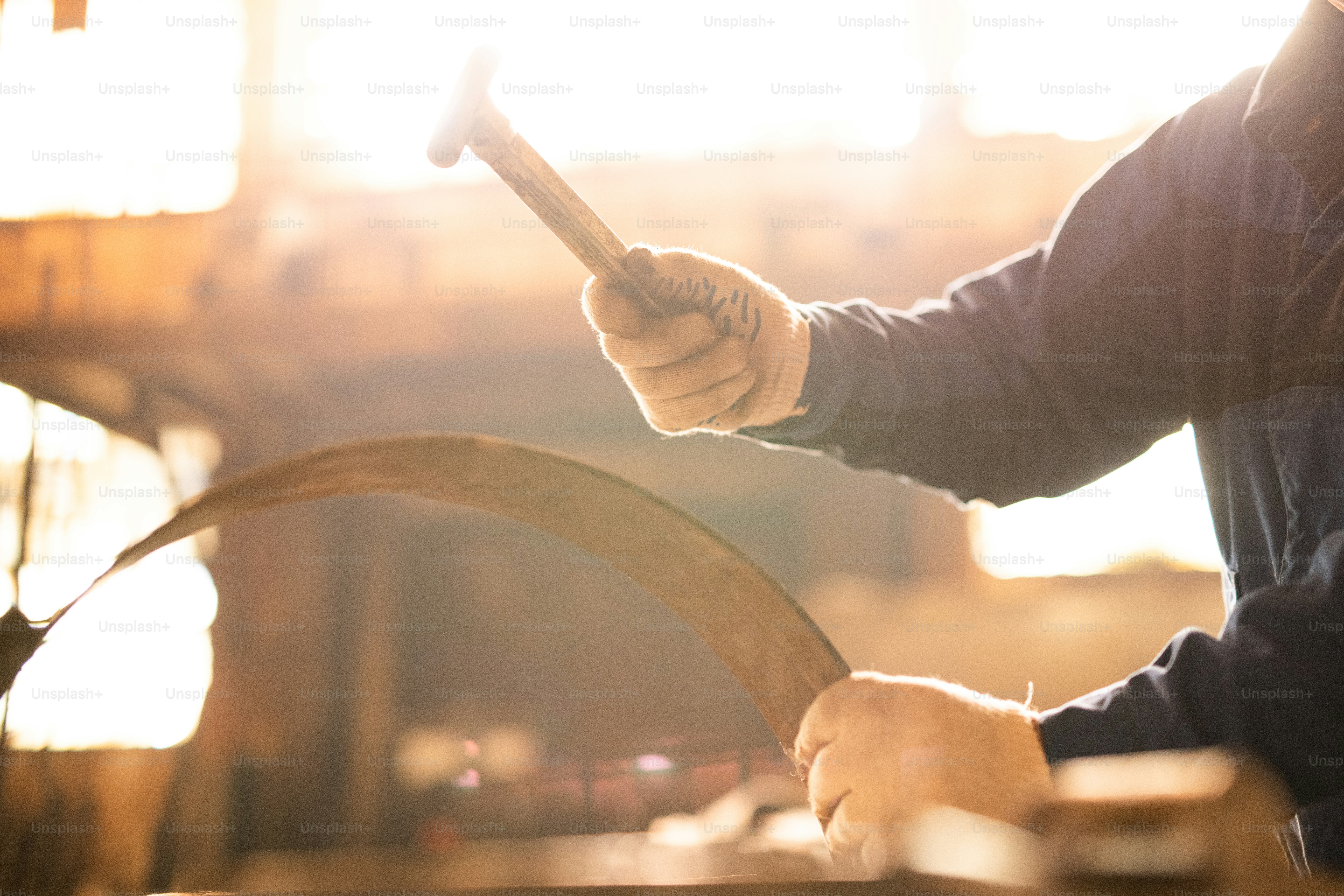 Contemporary engineer in workwear and gloves holding hammer over curve metallic workpiece