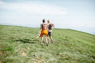 Hermosa pareja divirtiéndose, corriendo juntos en el prado verde, mientras viajan por las montañas durante el verano